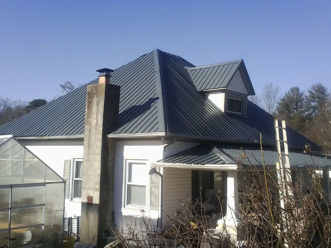 Dark blue standing seam metal roof on a white farmhouse with dormer — Slate & Tile Roof Repair by Roofing Brothers in Rural Valley