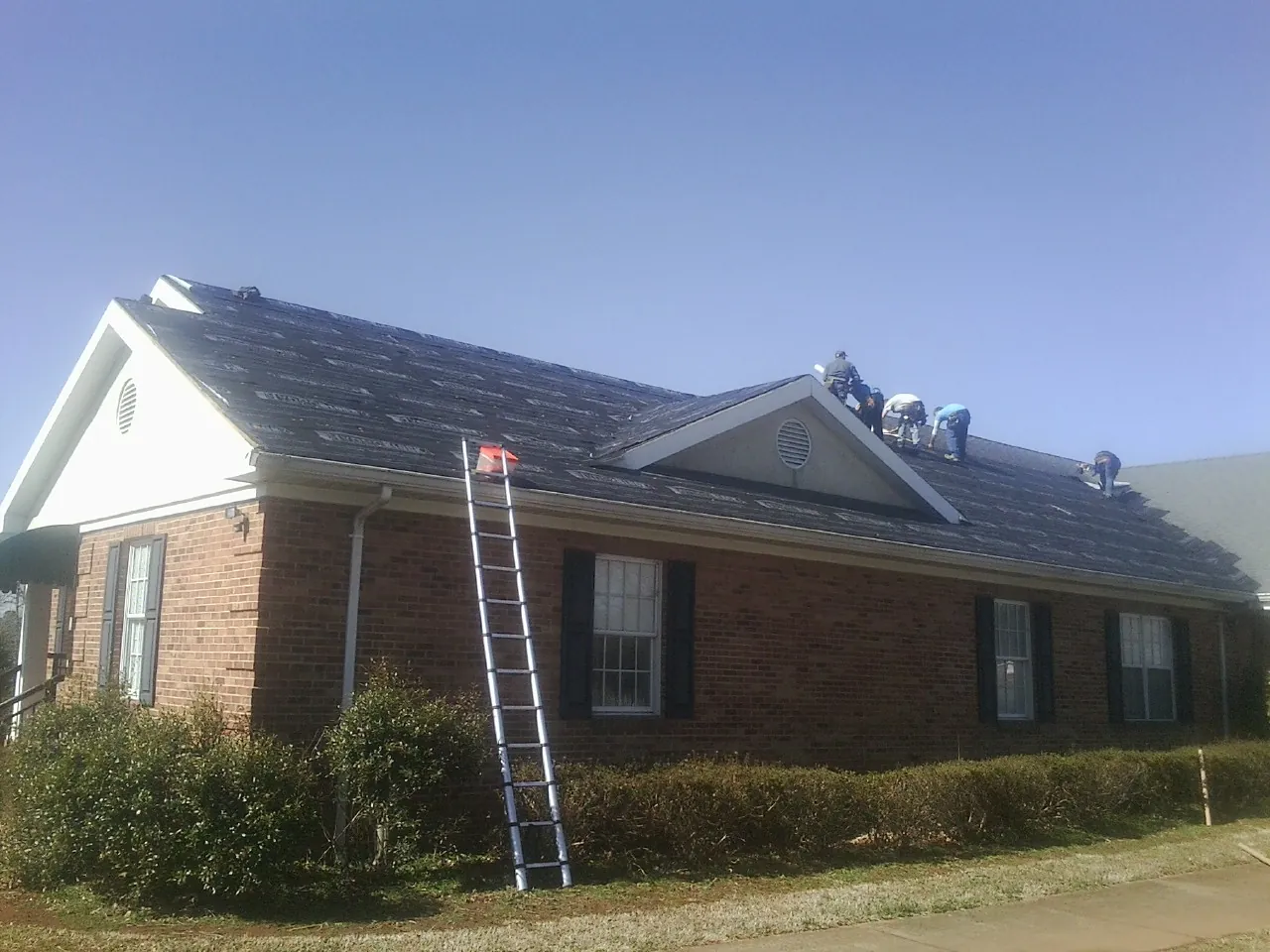 Crew tearing shingles off a brick ranch roof with a ladder set — Emergency Roof Repair work by our crew in Rural Valley