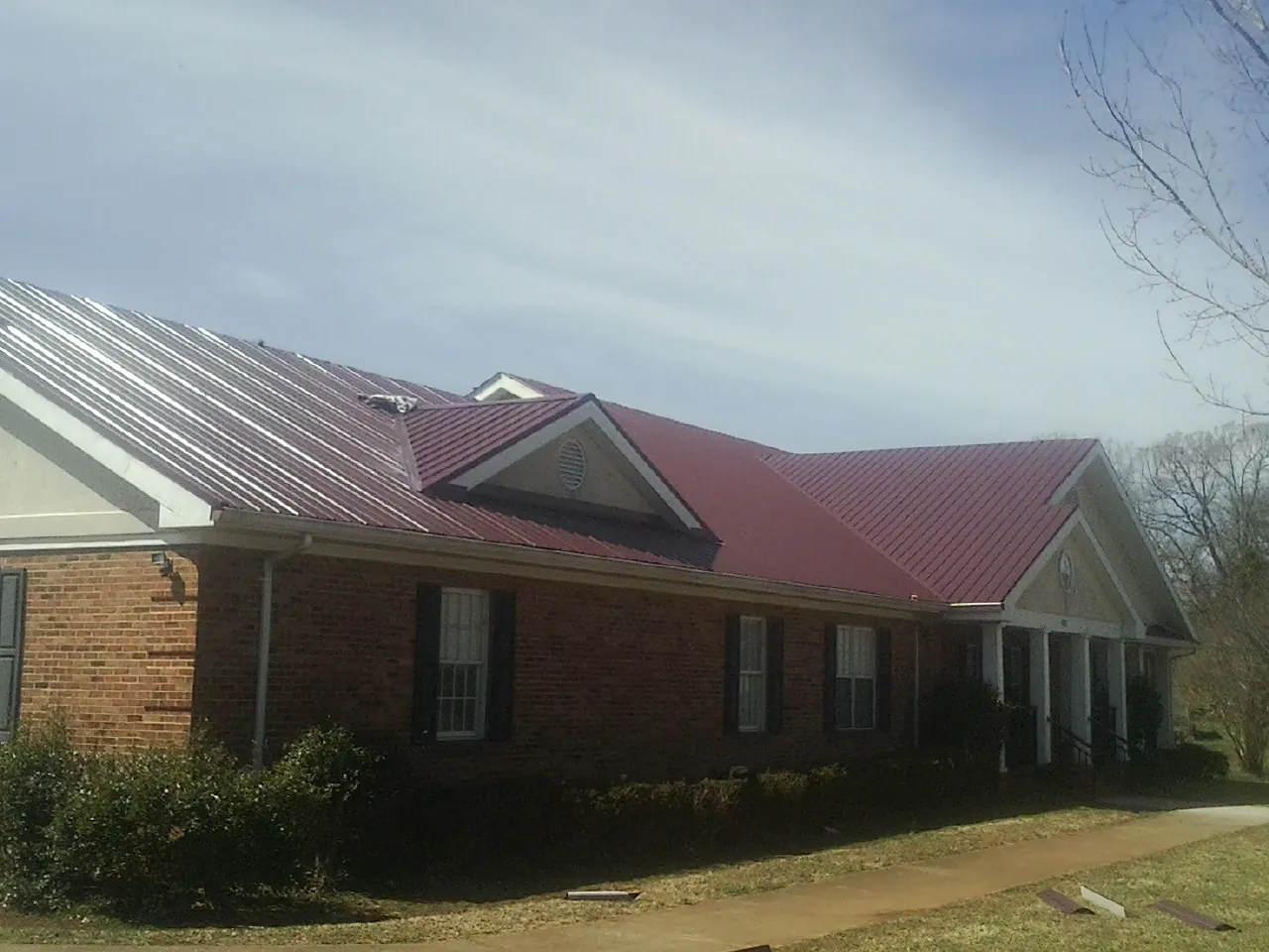 Red metal roof with gabled entries on a long brick building, from a Hail Damage Roof Repair job in Rural Valley
