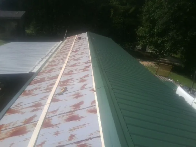 Old rusted panels beside newly installed green metal roofing — Wind Damage Roof Repair by Roofing Brothers in Rural Valley