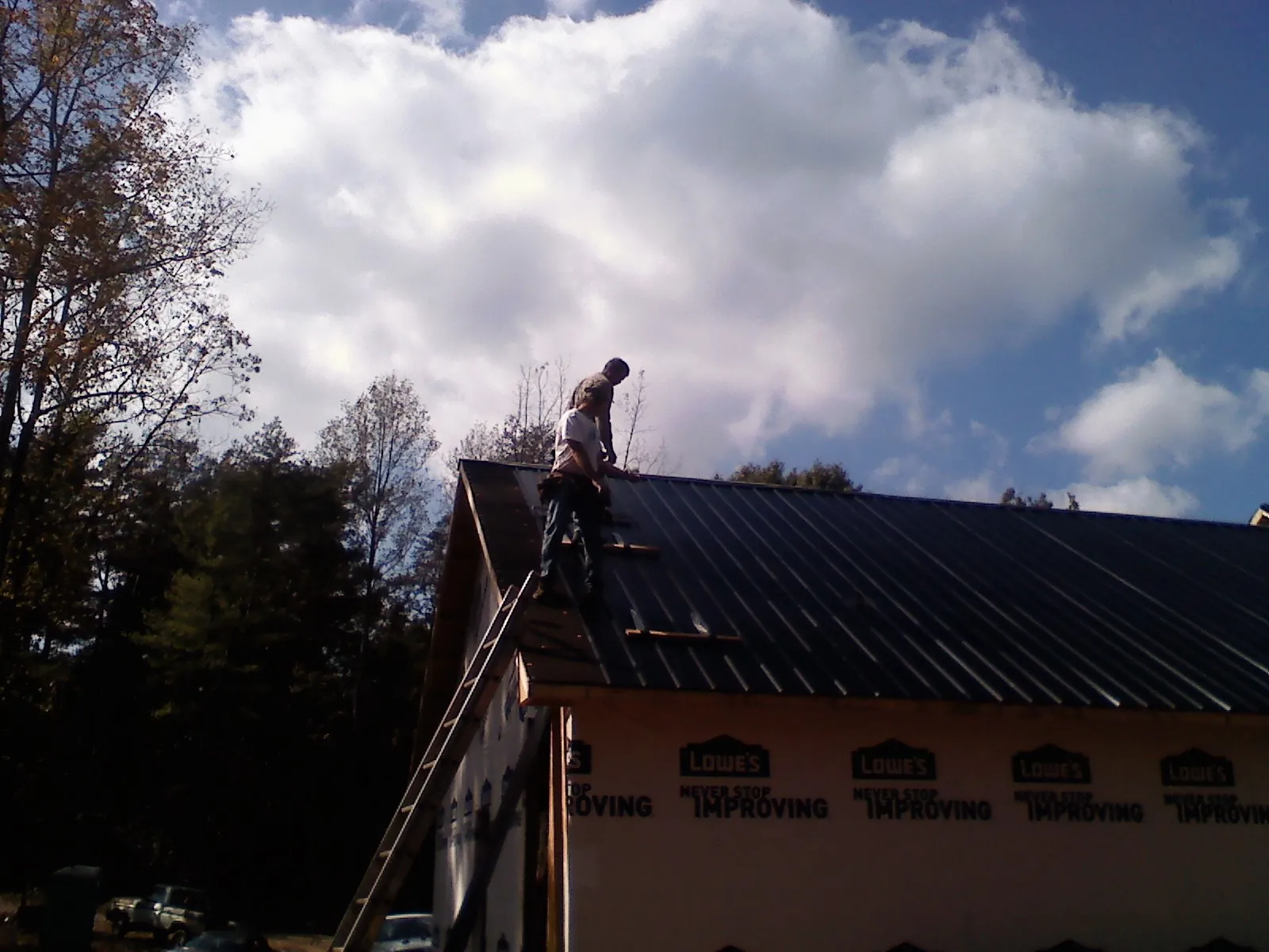 Roofer fastening dark metal panels high against a cloudy sky, from a Roof Inspection job in Rural Valley