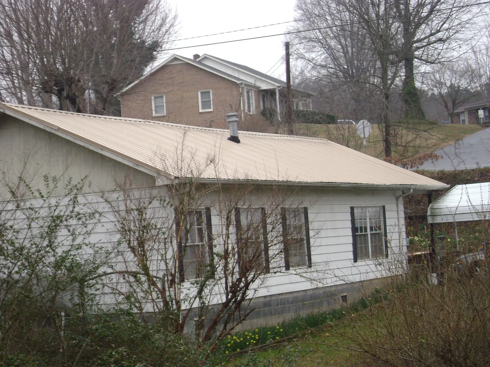 Tan metal roof on a white sided house set into a hillside — Commercial Roofing by Roofing Brothers in Rural Valley