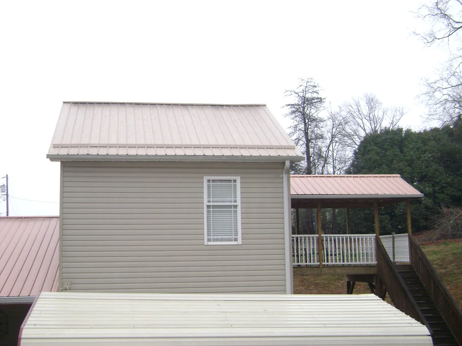 Tan metal roofs on a two story addition and attached porch, from a Roof Replacement job in Rural Valley